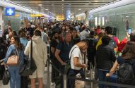 Fila extensa de pessoas em saguão de aeroporto lotado, com sinalização de serviços.