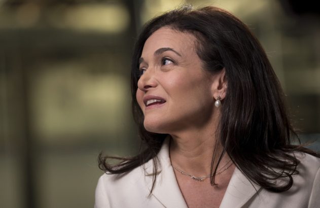 Retrato de mulher com cabelo escuro, olhando para cima e sorrindo. Veste blazer claro, brinco de pérola e colar.