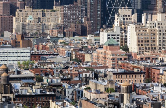 Paisagem urbana densa com edifícios de tijolos, arranha-céus e torres d'água nos telhados.