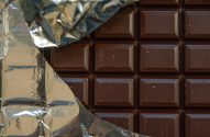 Barra de chocolate escura com embalagem de alumínio aberta, exibindo seus quadrados.