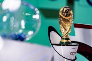 Troféu da Copa do Mundo FIFA Qatar 2022 e urna de sorteio com bolas azuis, fundo verde.