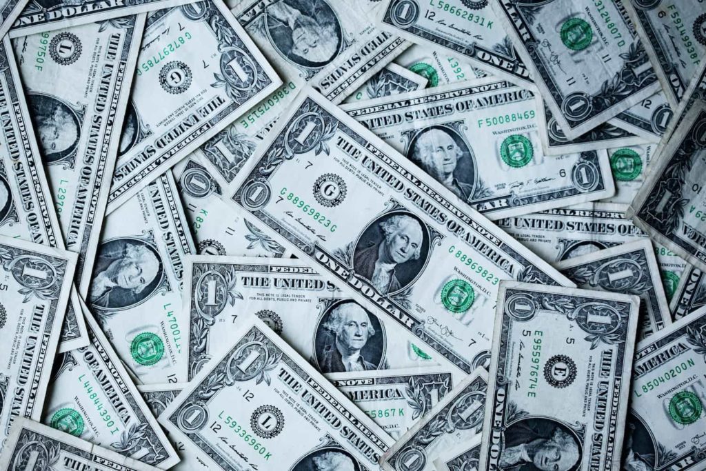 A imagem contém diversas notas de 1 dólar espalhadas em algum tipo de superfície.