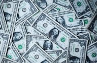 A imagem contém diversas notas de 1 dólar espalhadas em algum tipo de superfície.