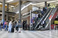 Terminal de aeroporto movimentado com pessoas em escadas rolantes e caminhando no saguão.