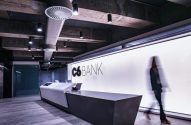 Recepção moderna do C6 BANK: balcão, logo em parede iluminada, pessoa borrada em movimento.