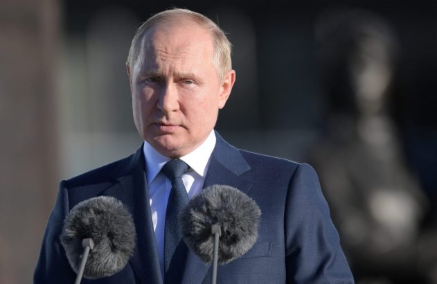 Vladimir Putin de terno, olhando à frente, com dois microfones à sua frente.