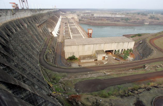 Vista aérea da usina hidrelétrica de Itaipu, com o imenso paredão de concreto, a casa de força e o rio.