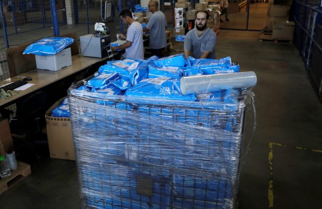 Funcionários em armazém processam e movimentam um palete grande de pacotes azuis embalados.