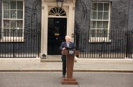 Boris Johnson em pronunciamento em pódio, à frente do nº 10 de Downing Street, prédio de tijolos escuros.