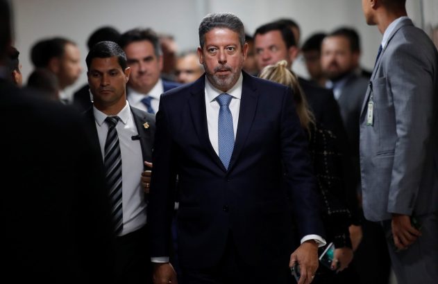 Homem de terno e gravata caminha em meio a um grupo de pessoas, incluindo um segurança.