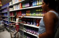 Menina em pé em carrinho de compras alcança produto na prateleira do supermercado. Mulher adulta a observa.