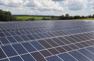 Inúmeros painéis solares em um campo, com vegetação e céu nublado ao fundo.