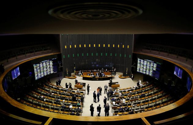 Vista aérea de um plenário parlamentar brasileiro, com membros em sessão e telas de votação.