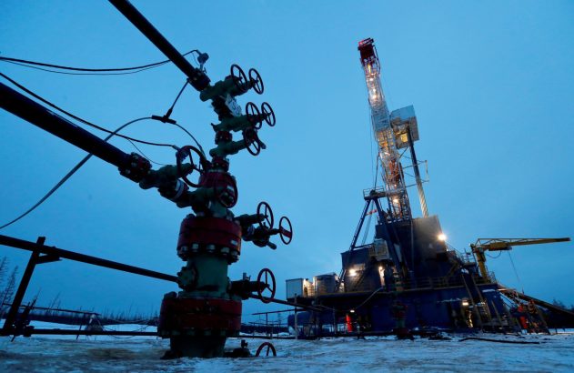Sonda de petróleo iluminada e válvulas de poço em ambiente nevado ao anoitecer.
