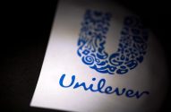 Logotipo azul da Unilever (símbolo e nome) em papel branco, parcialmente iluminado.