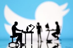 Silhuetas de pessoas trabalhando em computadores. Fundo azul com logo do Twitter desfocado.