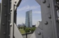 Edifício moderno de vidro e aço ao centro, com skyline ao fundo, enquadrado por estrutura metálica cinza com rebites.