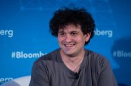 Homem Sam Bankman-Fried sorrindo, cabelo cacheado, camiseta cinza, em evento da Bloomberg.
