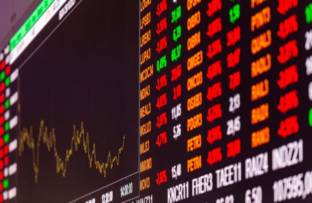 A imagem mostra, de perto, o telão da B3 com diversos tickers de ativos e suas variações de valor.
