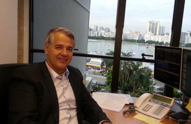 Homem sorrindo em escritório com vista para baía e cidade.