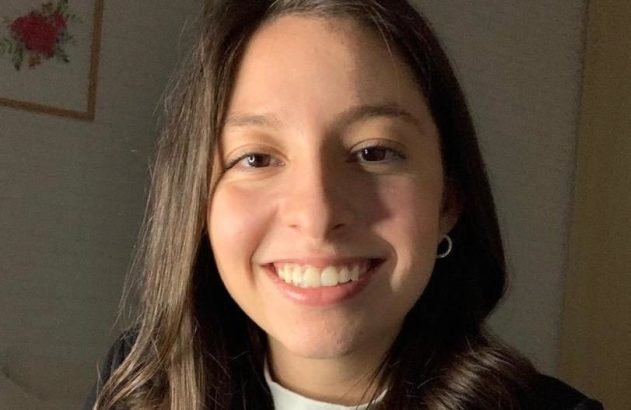 Retrato de perto de uma jovem sorrindo para a câmera, com cabelo castanho comprido.