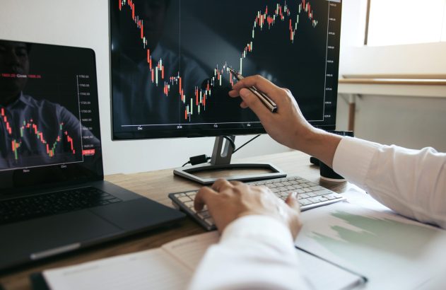 Homem aponta para tela de computador com gráfico de ativos