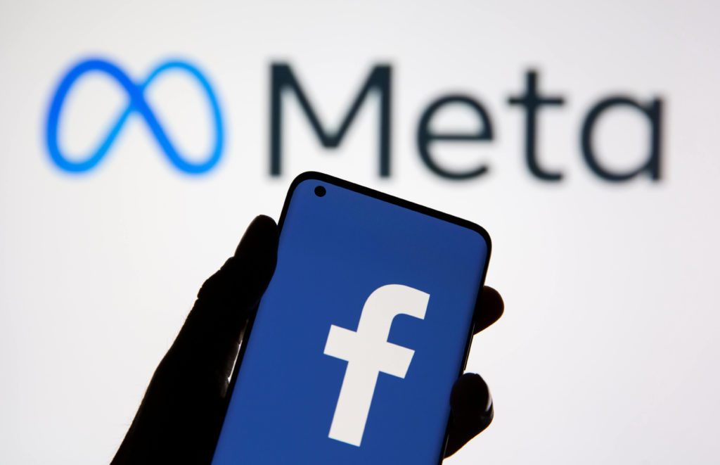 Mão segurando um celular com logo do Facebook