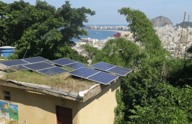 Painéis solares em telhado verde com vista para cidade litorânea.
