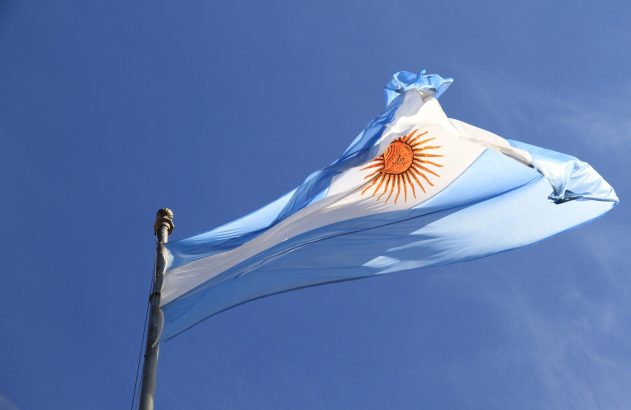 Bandeira da Argentina tremulando contra céu azul, com o Sol de Maio.