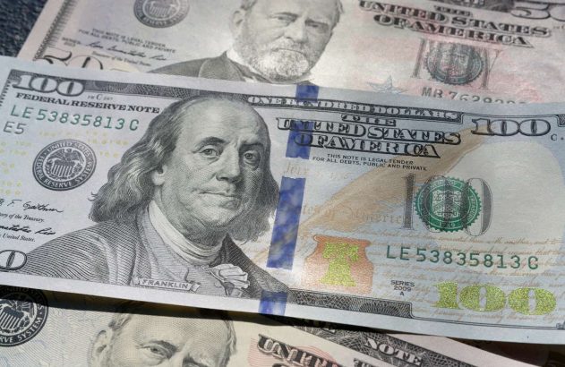 A imagem mostra uma nota de 100 dólares, posicionada acima de duas notas de 50 dólares. (Foto: Unsplash / Colin Watts)
