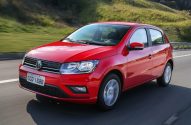 Carro hatch vermelho da Volkswagen em movimento em uma rodovia, com paisagem verde ao fundo.