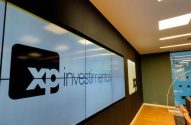 Ambiente de escritório moderno com grande painel de vídeo exibindo 'XP Investimentos' e logo XP.