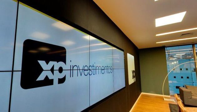Ambiente de escritório moderno com grande painel de vídeo exibindo 'XP Investimentos' e logo XP.