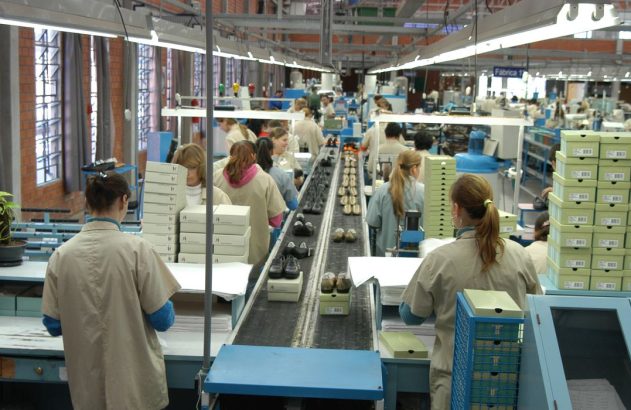 Fábrica de calçados: operárias montam e embalam sapatos em linha de produção com esteira e caixas.