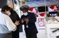Funcionário da Casas Bahia com máscara mostra celular a dois clientes com máscara em loja de eletrônicos.