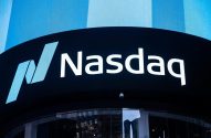Letreiro e logo Nasdaq iluminados em edifício escuro com painel azul brilhante acima.