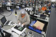 Pessoas em fábrica de eletrônicos montando notebooks em linha de produção.