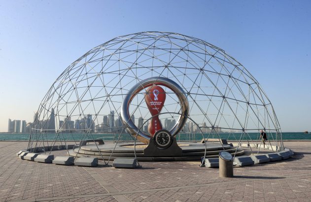 Cúpula geodésica com relógio da Copa do Mundo FIFA 2022 e paisagem urbana de Doha, Catar, ao fundo.
