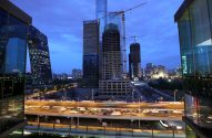 Skyline de cidade ao anoitecer: o prédio CCTV, arranha-céus e construções, com tráfego intenso na rodovia elevada.