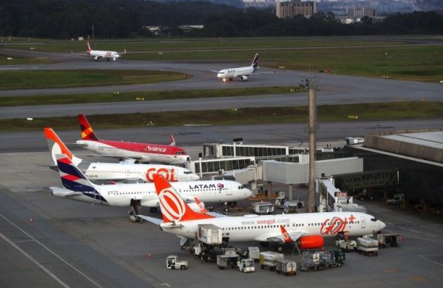 Vista aérea de pátio de aeroporto com aviões GOL, LATAM, Avianca estacionados e taxiando, com jet bridges.