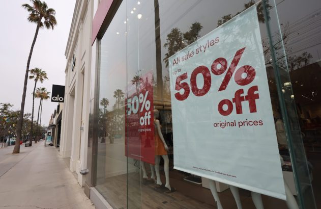 Vitrine da loja Alo com cartazes de 50% de desconto. Manequins dentro e palmeiras na rua.