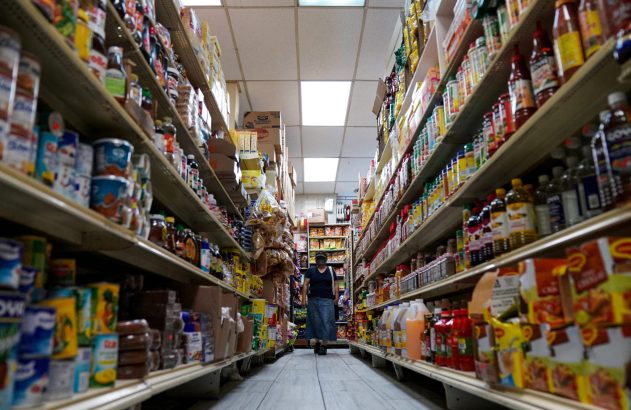 Pessoa caminhando em corredor de mercearia com prateleiras cheias de produtos.