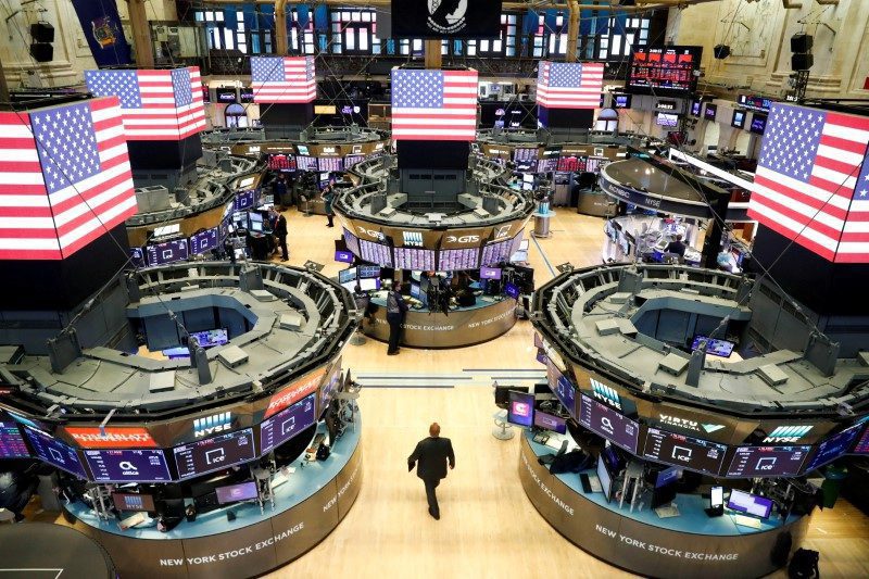 Vista aérea do pregão da Bolsa de Nova York com telas de negociação, bandeiras dos EUA e um homem caminhando.