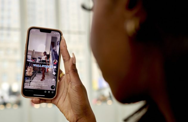 Mão de pessoa segurando celular. Na tela, vídeo "23 YEAR OLD BLACK GIRL WORKING ON WALL STREET".