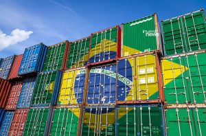 Contêineres de carga empilhados, muitos com a bandeira do Brasil e um com o logo 'invest news'.