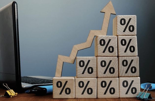 Seta e cubos de porcentagem em tendência de crescimento, representando a taxa de juros do cartão de crédito, sobre uma mesa com notebook,um marca texto e dois clipes. (Foto: Adobe Stock / Vitalii Vodolazskyi)