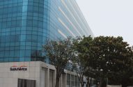 Edifício moderno de fachada azul-espelhada com o logo SulAmérica e árvores no primeiro plano.