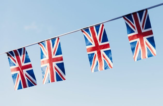 Quatro bandeiras Union Jack penduradas em varal, sob céu azul.