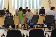 Pessoas em estações de computador. Um homem atende uma mulher e uma criança. Outros usam os computadores.