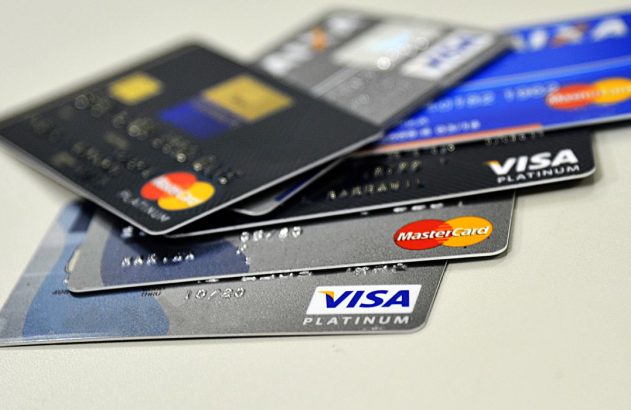 Diversos cartões de crédito, Visa Platinum e Mastercard, empilhados sobre uma superfície clara.
